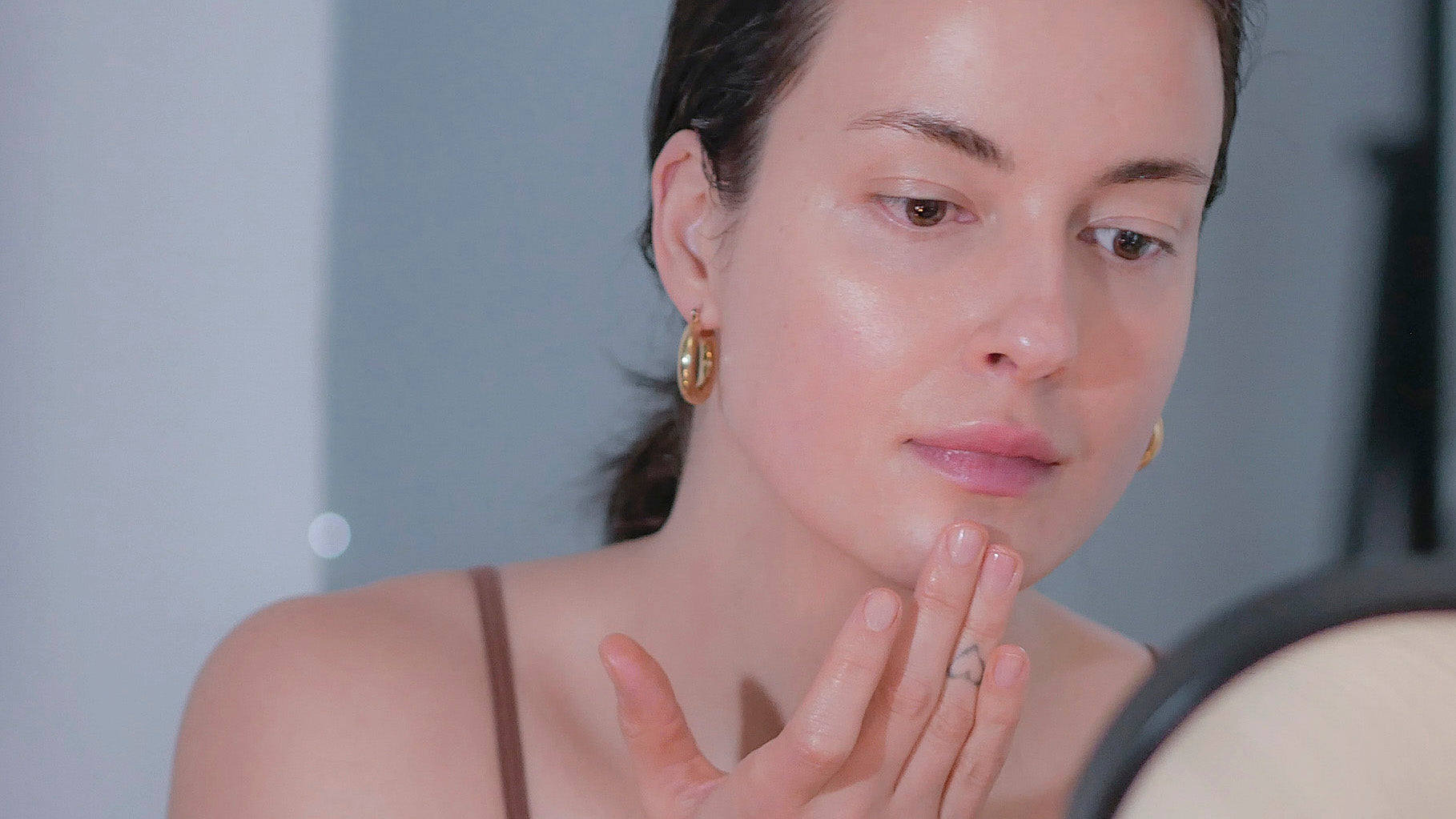 Woman with hair pulled back applying restorative night serum to face.