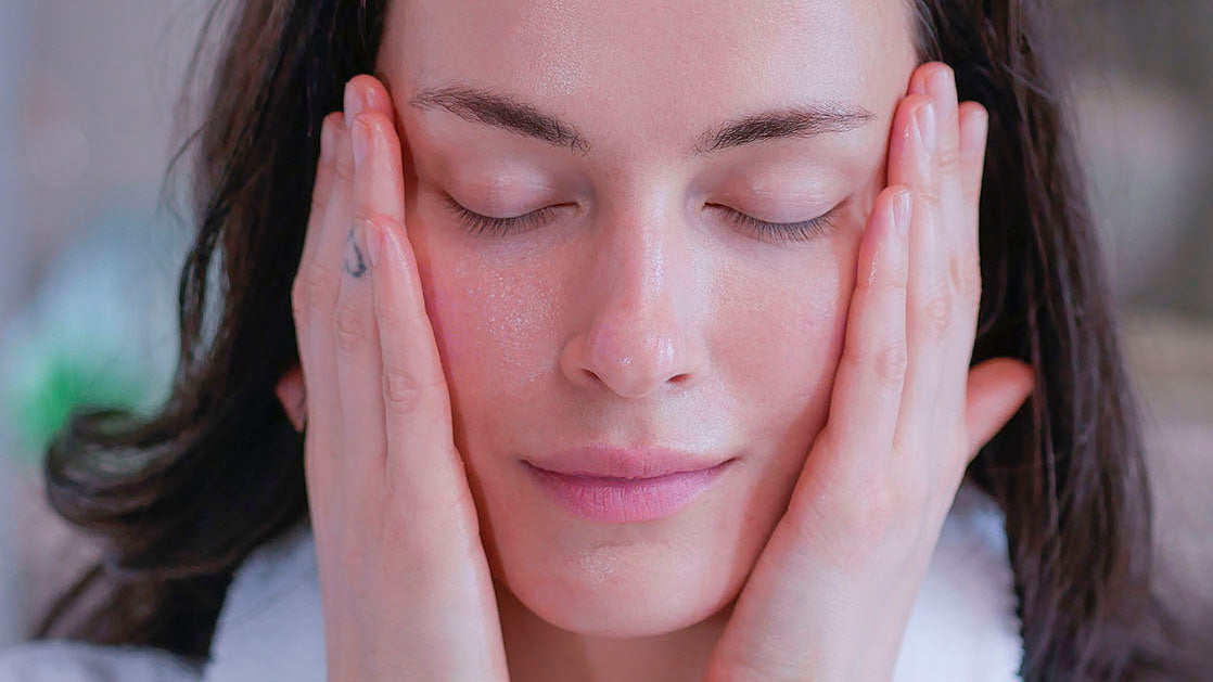 A woman with dark hair wearing a white fluffy bathrobe applying organic facial toner for the ultimate skin hydration.
