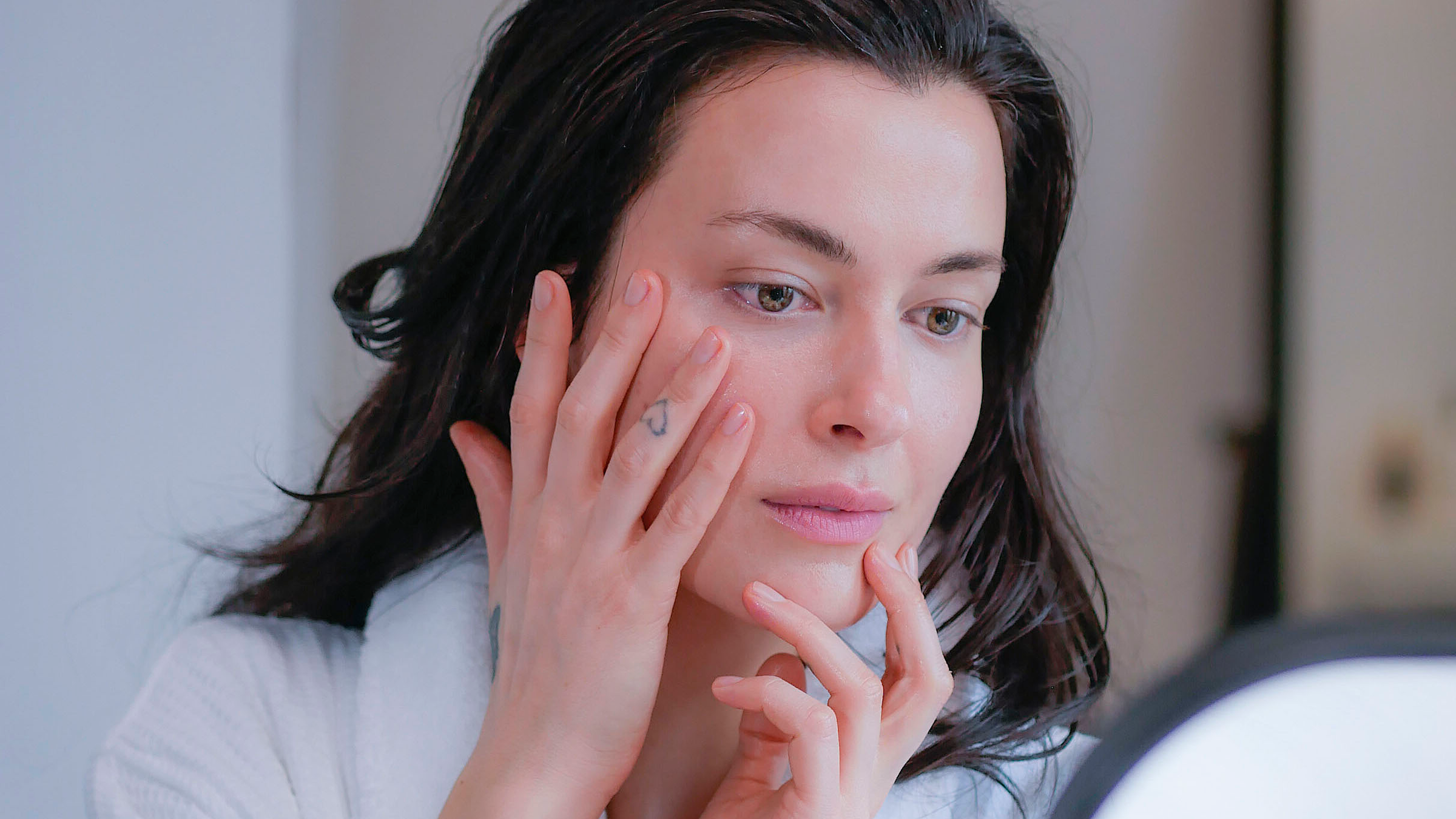 woman looking in mirror with hand on face