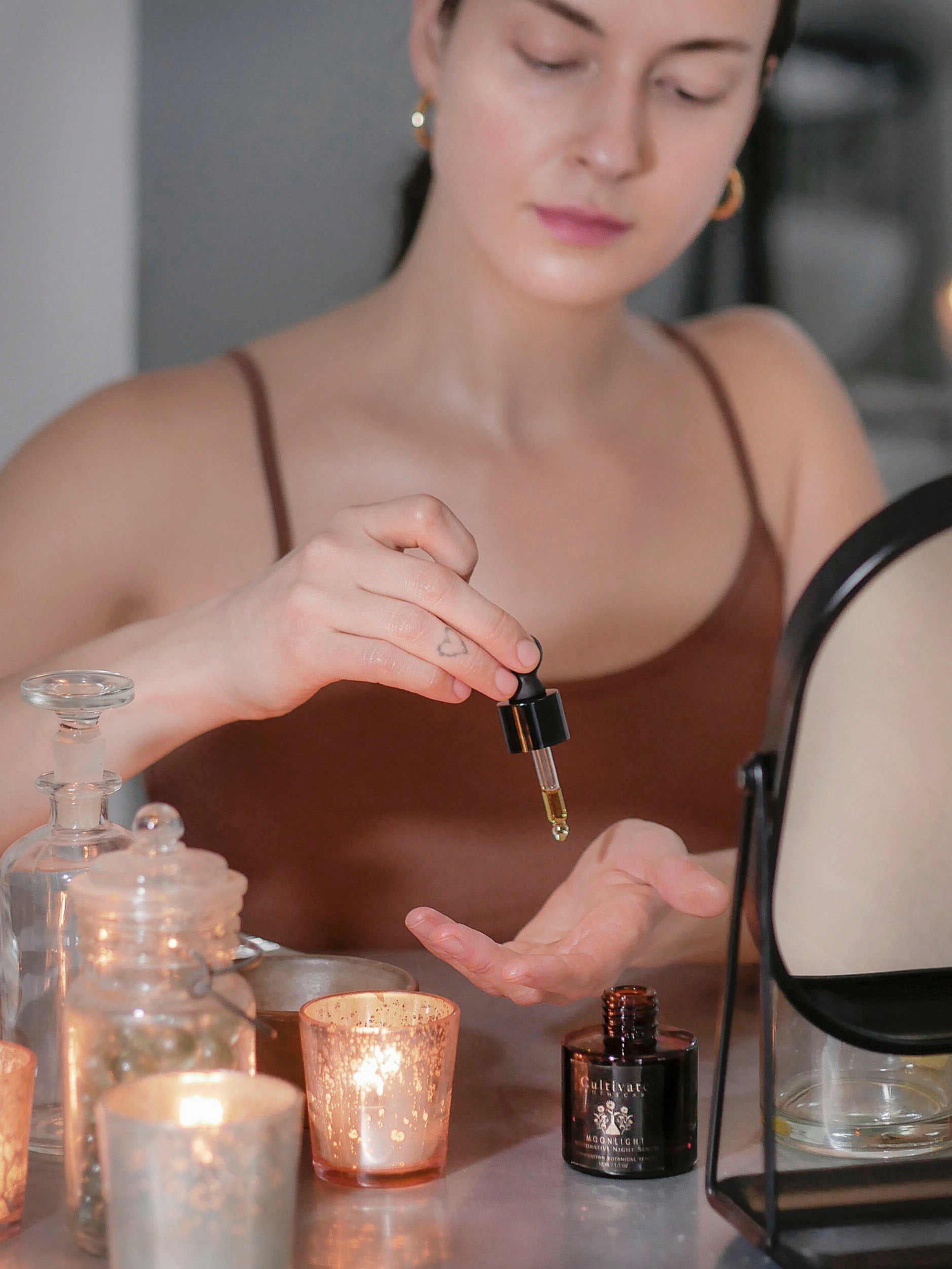 A woman in a brown tank top applying night repair serum for combination skin.