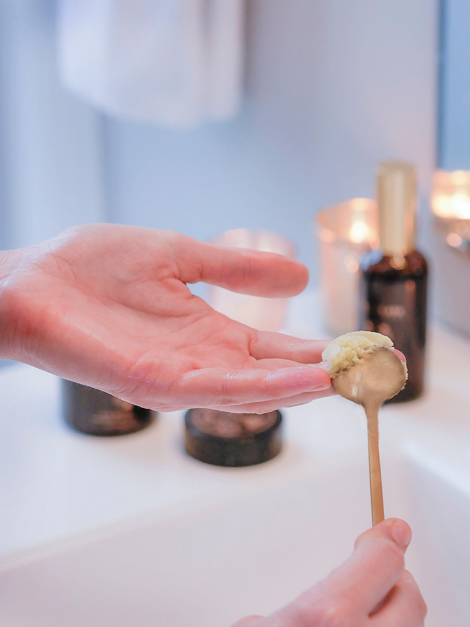 Woman scooping balm cleanser into palm of hand using a gold face mask spoon.