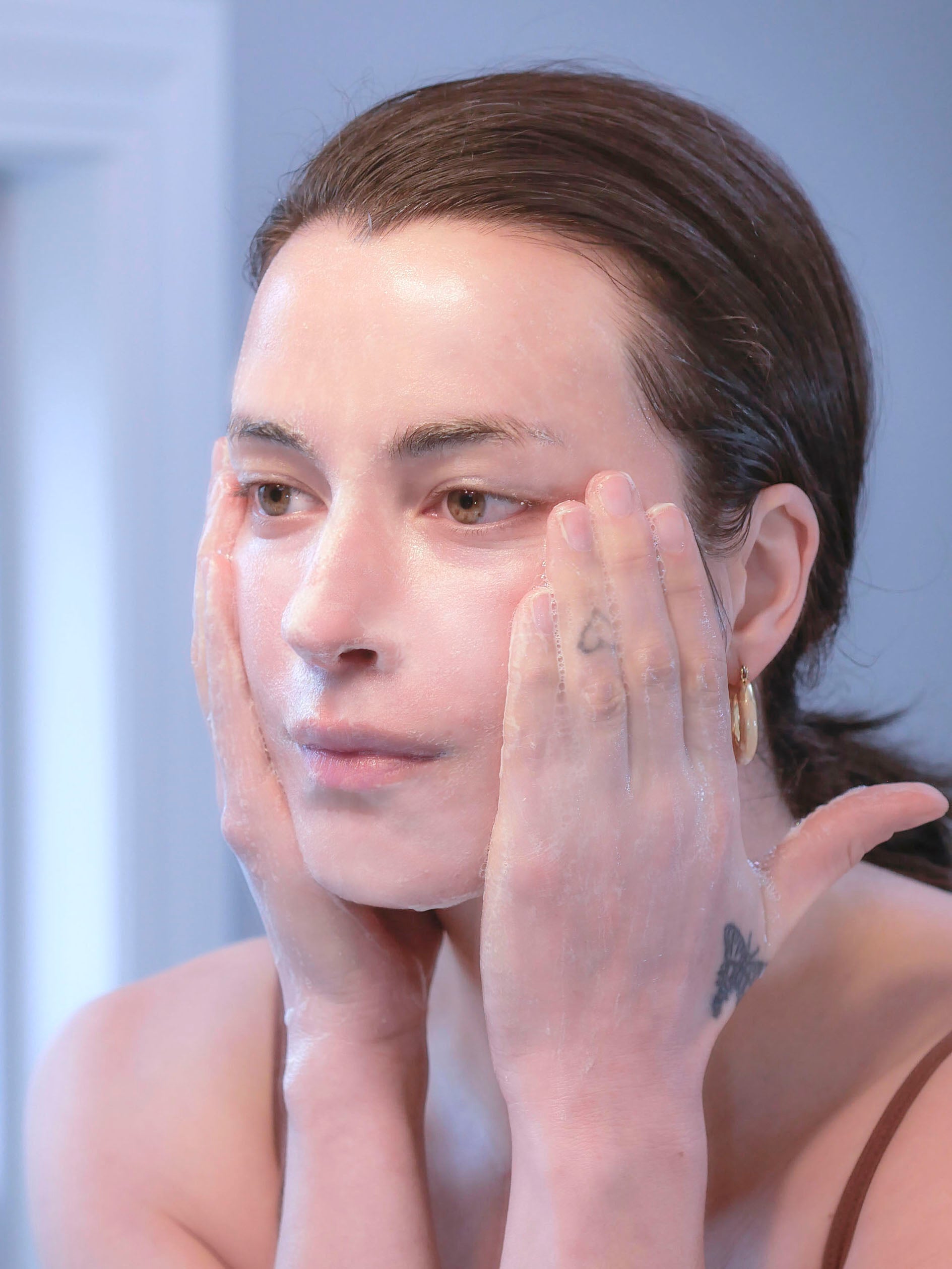 Woman with brown hair washing face with a non-toxic balm cleanser.