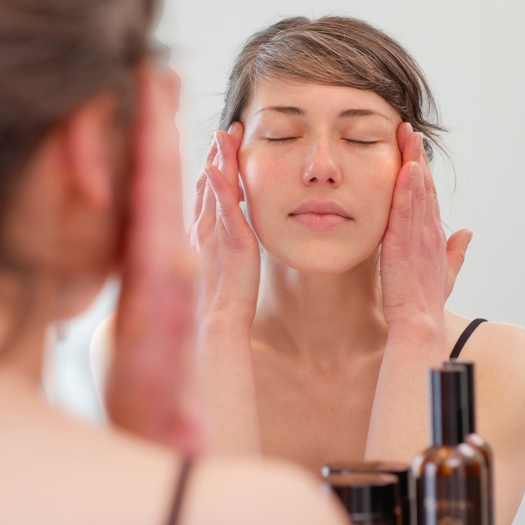 Woman with dark hair pulled back applying custom skincare products thanks to a personalized skincare quiz.