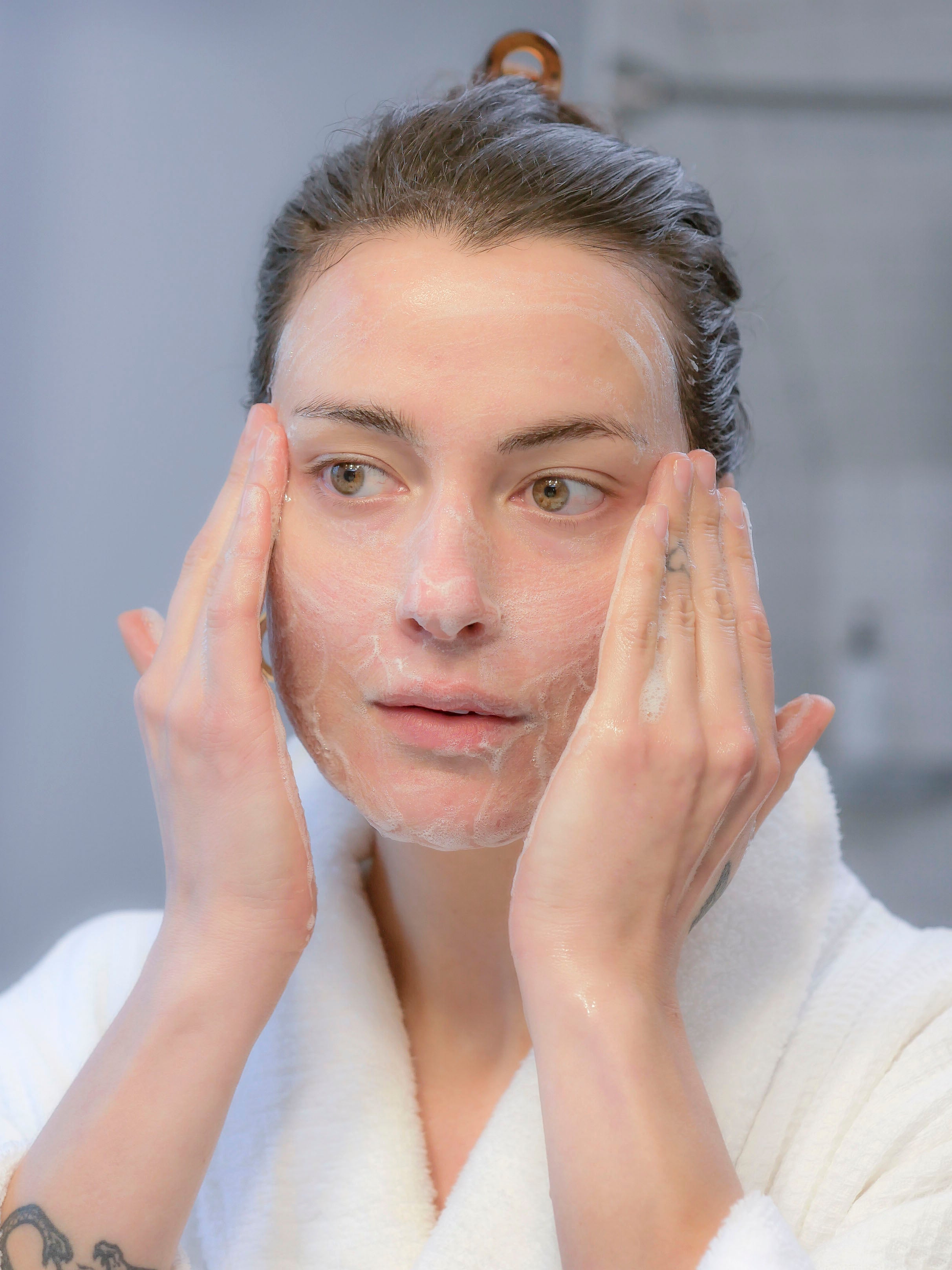 A woman with brown hair using Radiance by Cultivate Apothecary, a botanical daytime face cleanser.