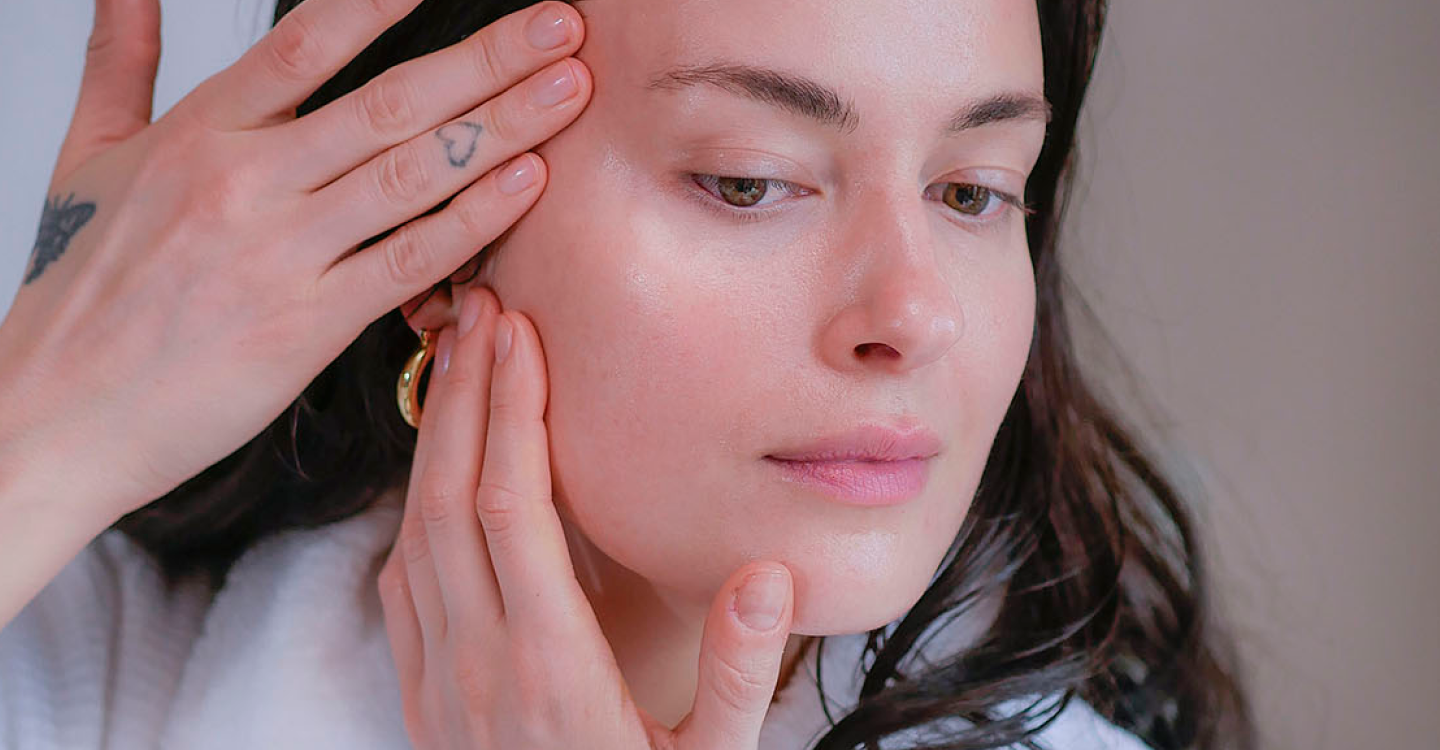 Woman with dark hair in a white fluffy bathrobe doing her skincare routine and skincare rituals.