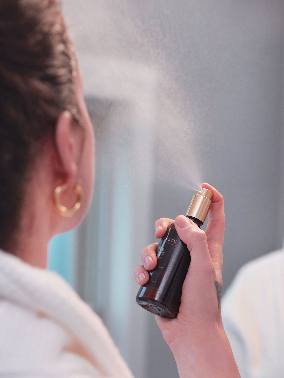 Side view of a woman applying a mist of the natural facial toner for ultimate skin hydration.