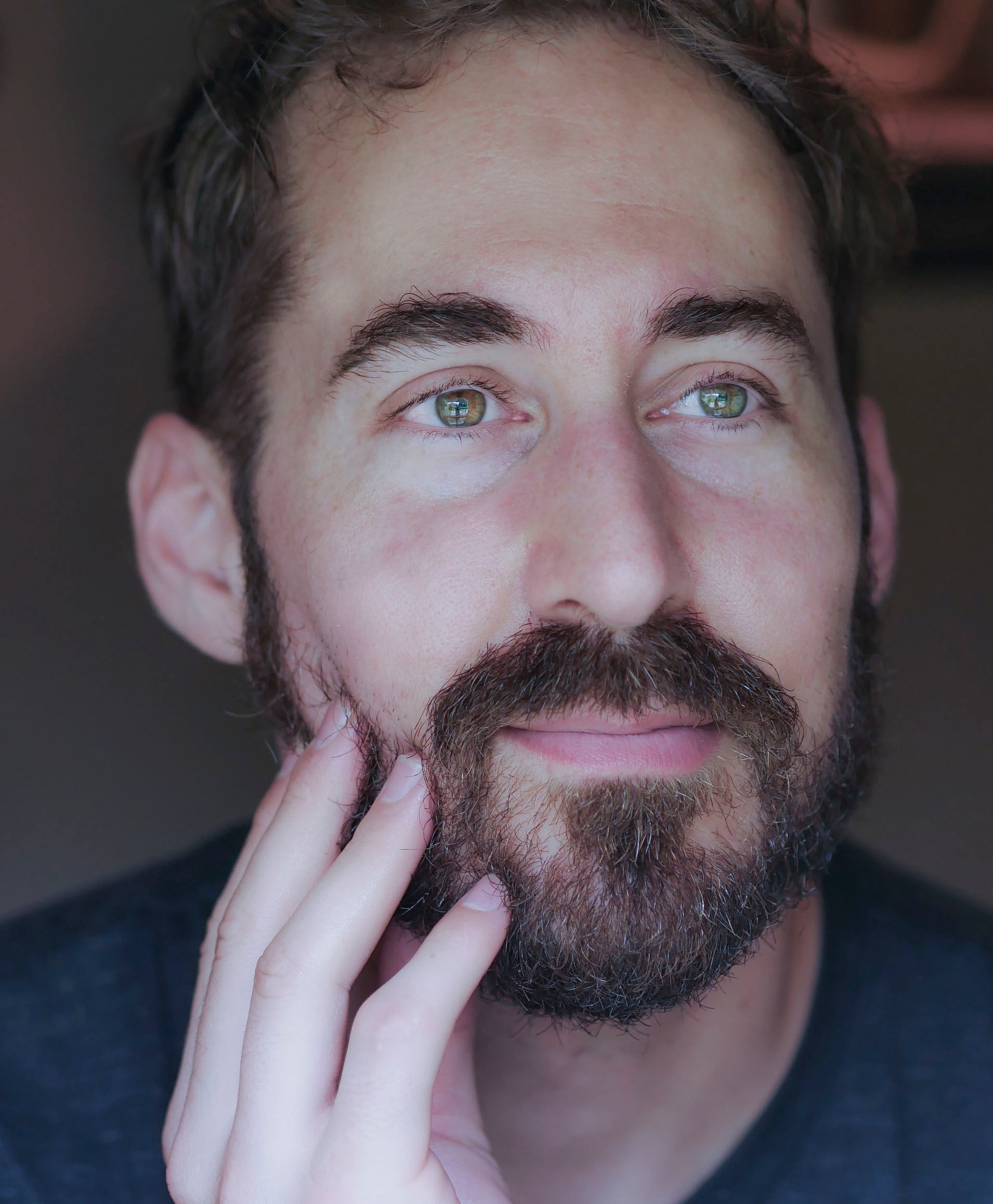 A man with brown hair and a beard after applying Evolution men's facial serum.