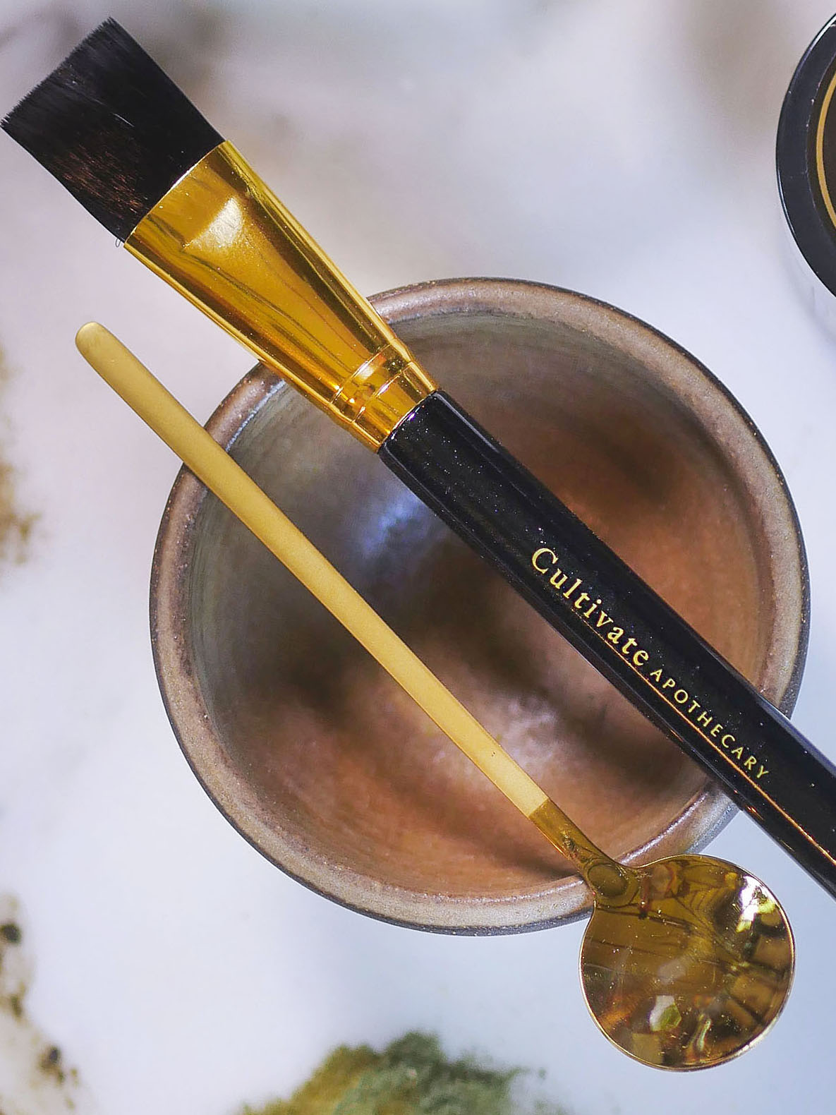 Face mask brush resting on a face mask bowl with a gold face mask spoon.