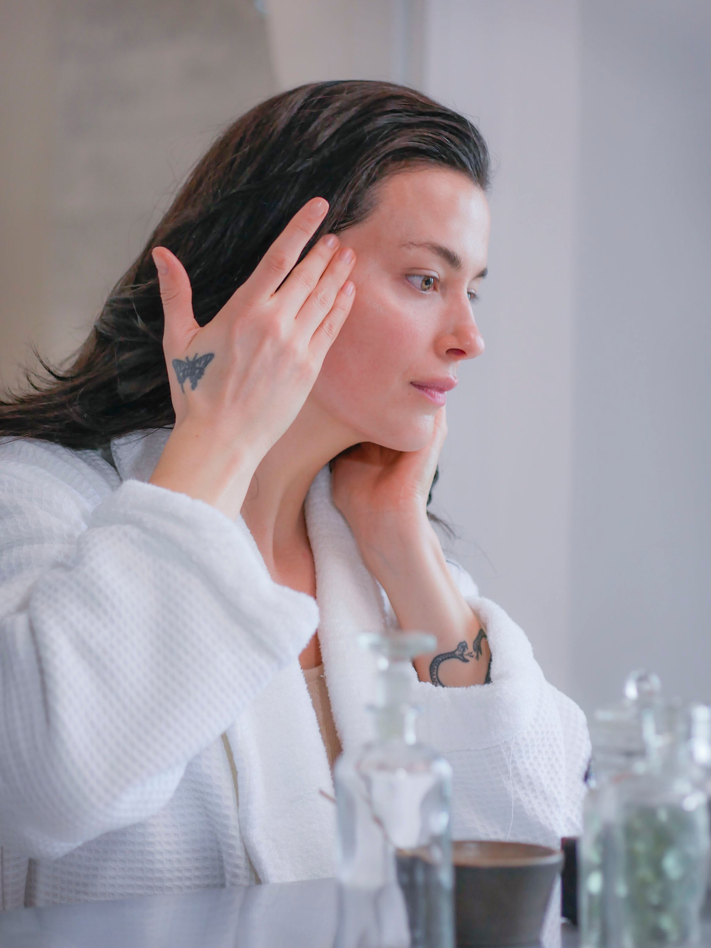 A woman in a white waffle bathrobe applying the best face serums for sensitive skin.
