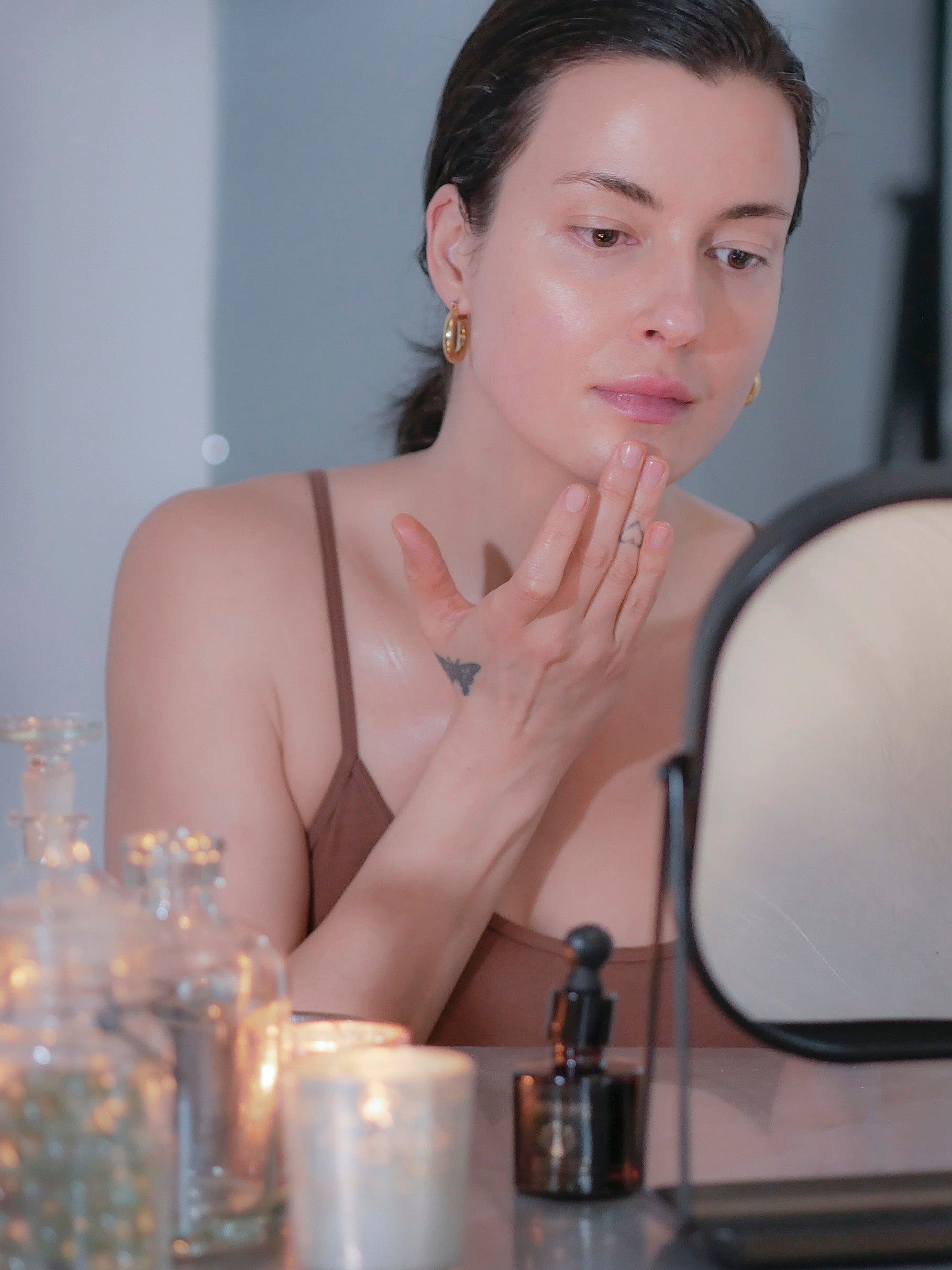 Woman in a brown tank top with hair pulled back applying night face serum for dry skin.