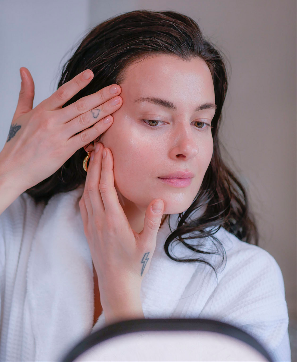 Woman with dark hair in a white fluffy bathrobe doing her skincare routine and skincare rituals.