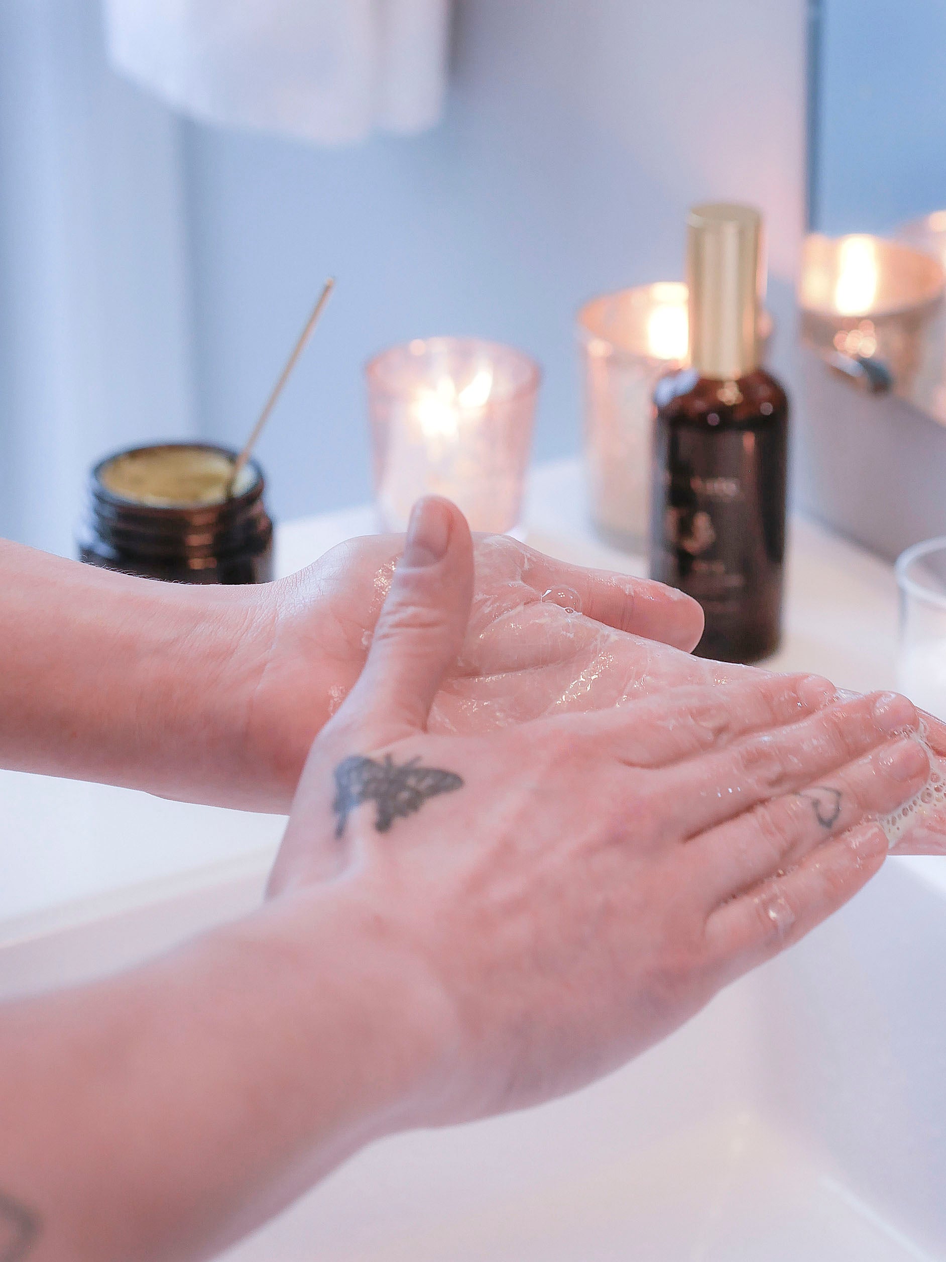 A woman with a butterfly tattoo and heart tattoo on her hands massaging a non-toxic cleansing balm between her hands.