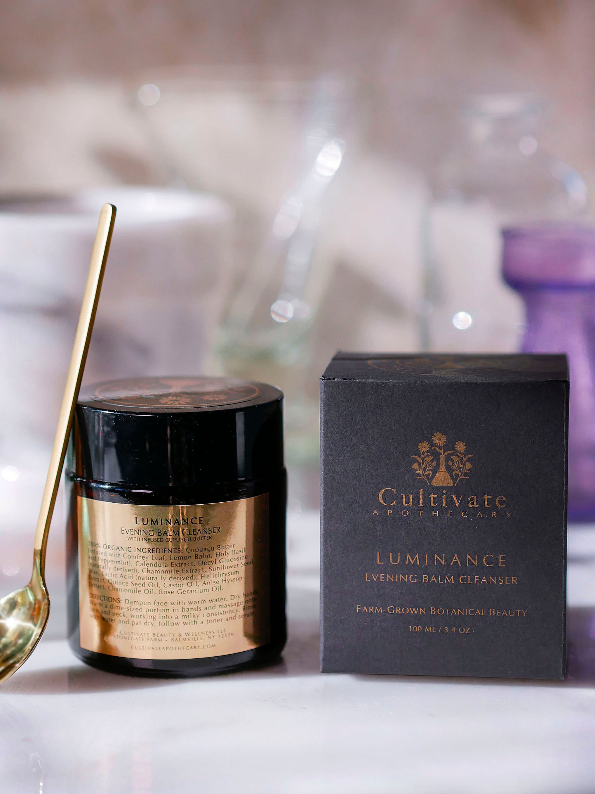 A gold face mask spoon leaning against the evening balm cleanser product box.